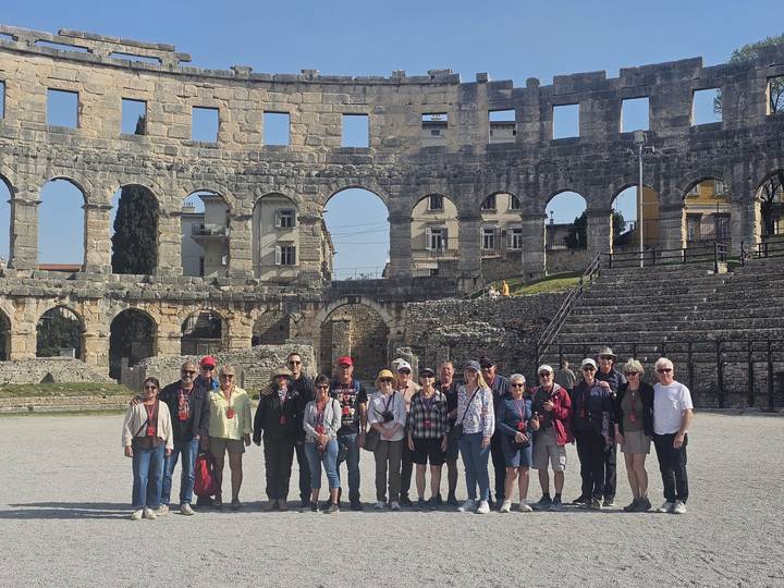 Large tour group posing inside the Roman amphitheatre surrounded by towering stone arches.