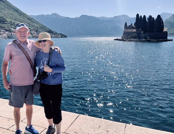 Couple smiling by shimmering bay waters with mountain backdrop and island church in Kotor.
