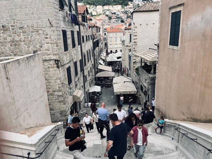 Stone staircase alley in Dubrovnik filled with tourists ascending between historic buildings.
