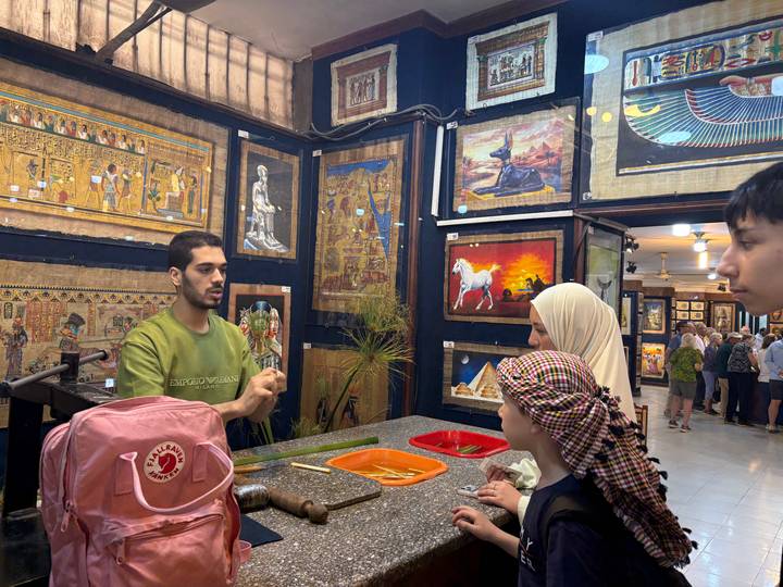 Papyrus art shop where a guide demonstrates painting techniques to an attentive family.