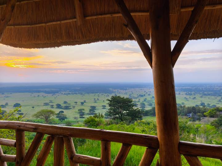View across open plains from a wooden lodge balcony at sunrise with soft pastel skies.
