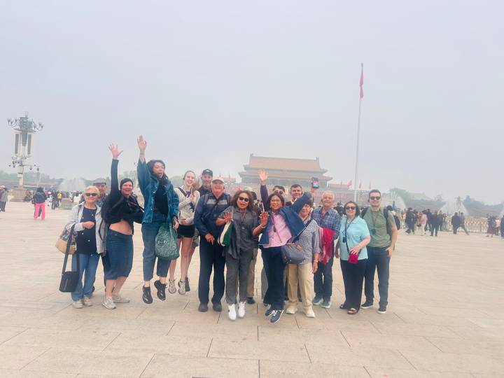 Tourists jump and pose in Tiananmen Square on a smoggy day with national flag behind.