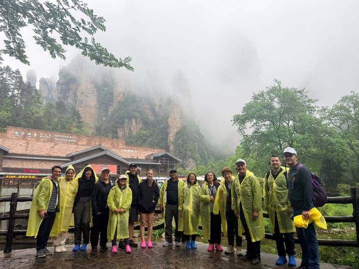 Group in yellow rain ponchos with misty sandstone spires rising behind them in a forest park.
