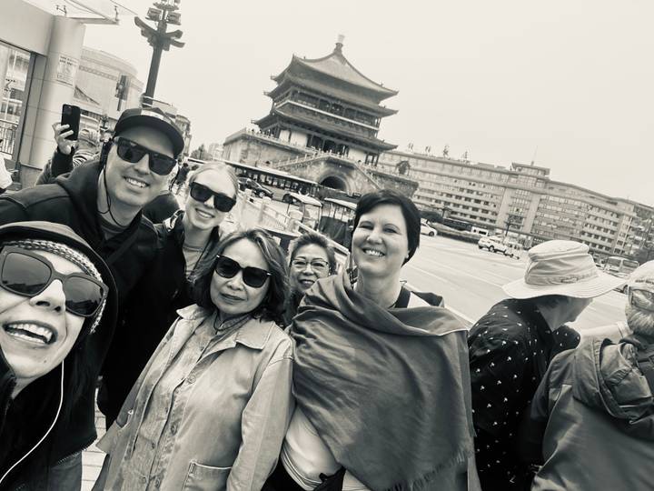 Black-and-white selfie of travelers in front of a historic Chinese tower at a busy city intersection.