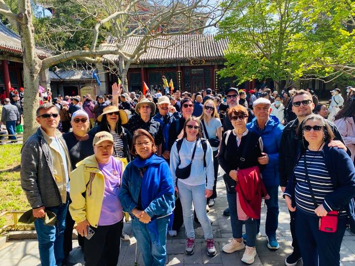 Large tour group gathers in a courtyard of a traditional Chinese complex amid many other visitors.