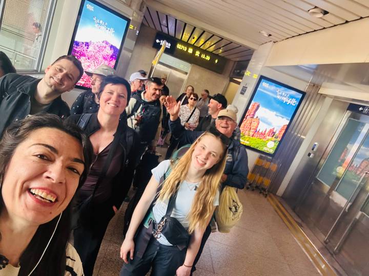 Cheerful group selfie inside a modern rail station corridor with digital signs overhead.