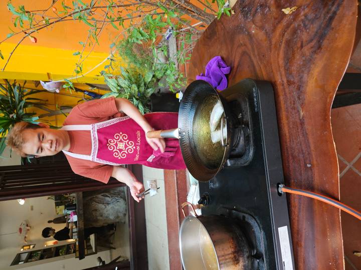 Cooking instructor fries spring rolls in a wok set on an outdoor stove during a class.