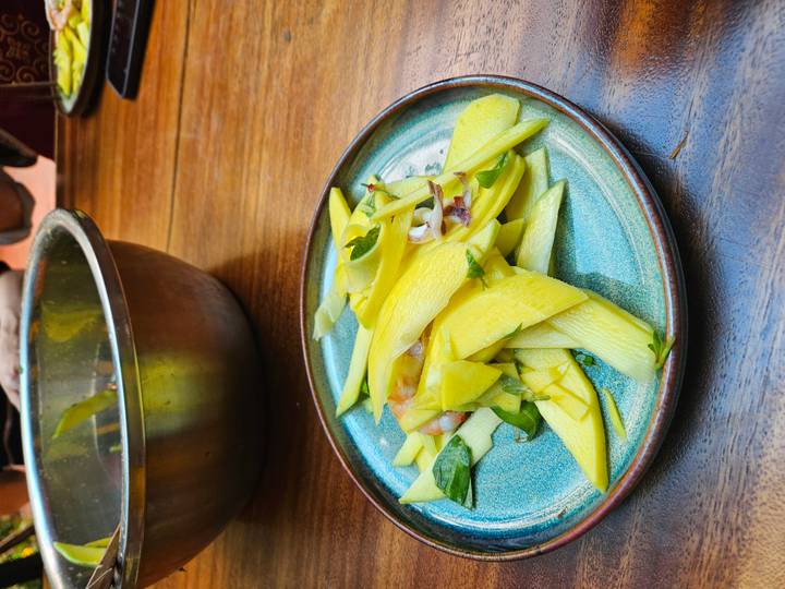 Fresh mango and herb salad arranged on a turquoise ceramic plate on a wooden table.