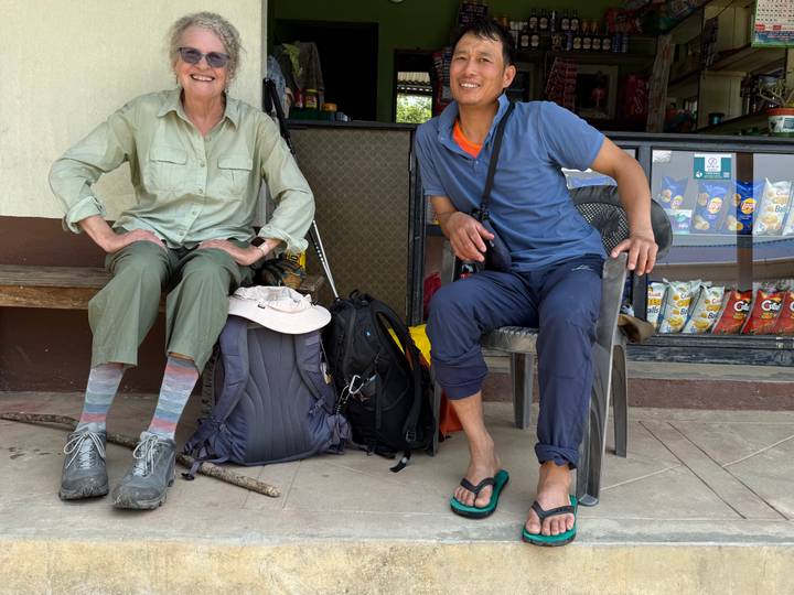 Trekker and local guide resting outside a small shop with backpacks and snacks around