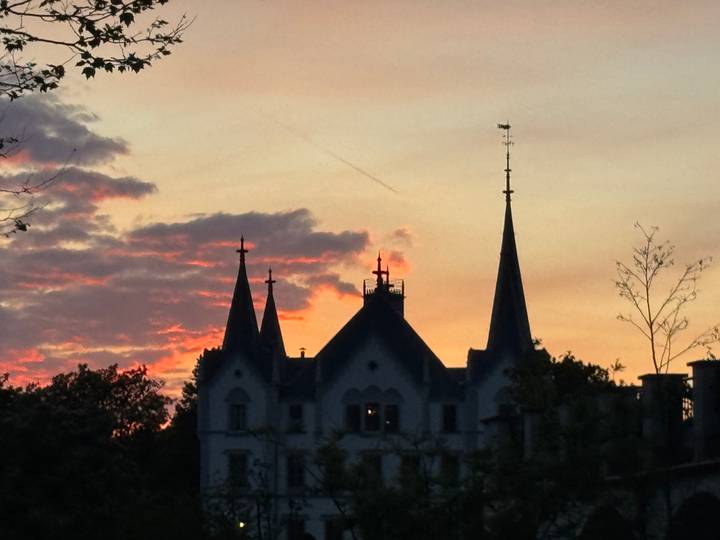 Silhouetted spires of a castle against a colorful sunset sky with streaks of clouds.