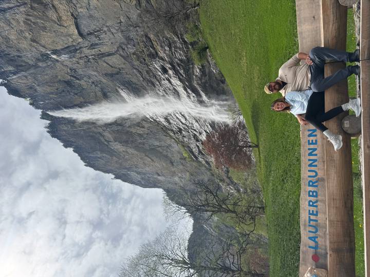 Couple sitting on a log with a tall waterfall and cliff face towering behind them in Lauterbrunnen.