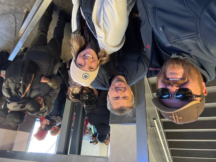 Selfie of travelers inside a busy alpine transport station with crowds in background.