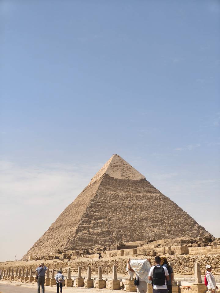 Pointed apex of a Giza pyramid stands against pale sky, highlighting weathered stones.