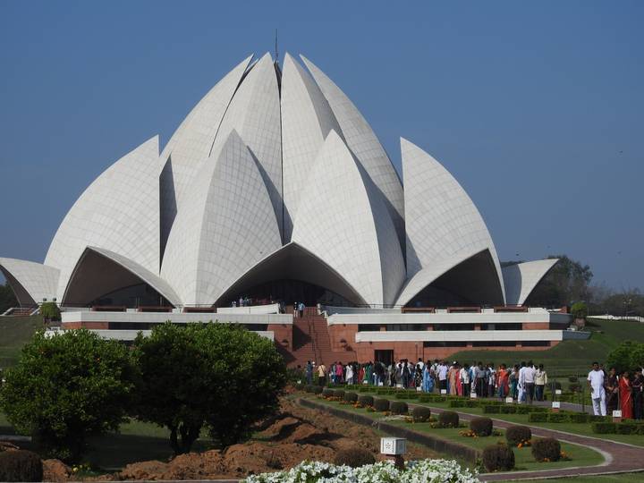 Crowds queue outside the white petal-shaped Lotus Temple set against clear blue Delhi sky.