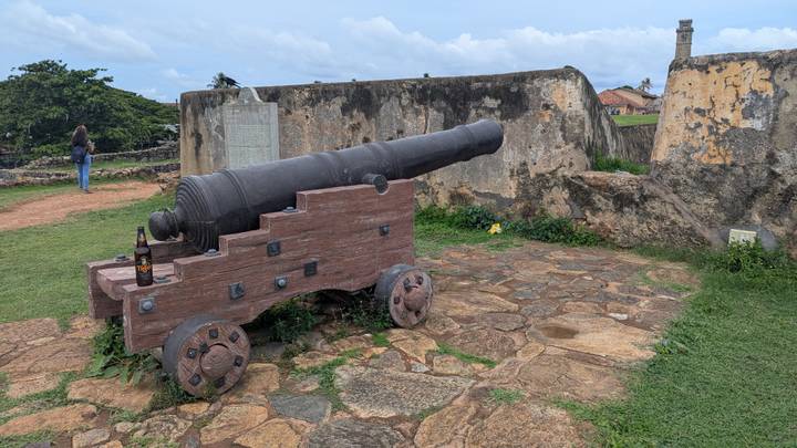 Old black cannon on a wooden carriage overlooks the ramparts of Galle Fort, with a beer bottle placed on it.