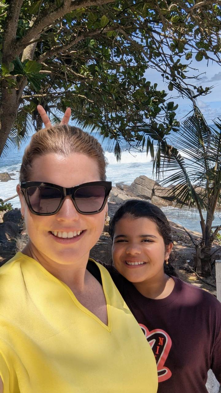 Smiling mother and daughter selfie with crashing Indian Ocean waves and palm fronds behind them.