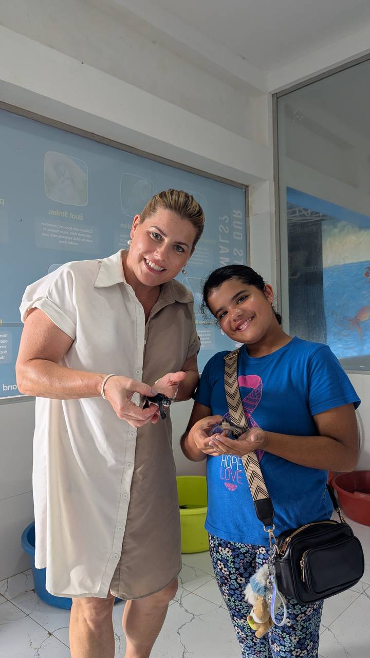 Adult and child proudly holding tiny sea turtles inside a conservation centre.