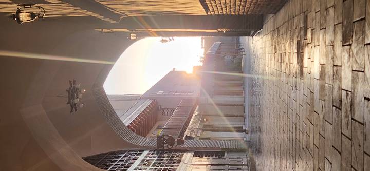 Narrow arched passageway paved with stone, morning sun streaming through the far arch creating lens flare.