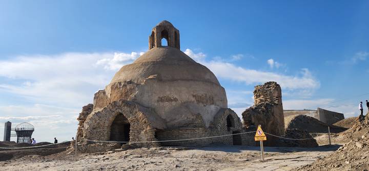Ancient stone-built domed bathhouse ruins under a vivid blue sky with protective rope barrier.