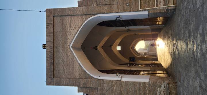 Long vaulted brick arcade glowing with early morning sunlight and lone figure in the distance.