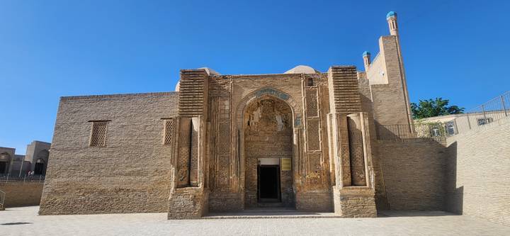 Stone-brick medieval mosque façade with arched entrance under a deep blue sky.