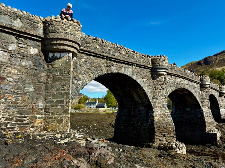 Close-up of the arched stone bridge spans with mountains and cottages framed by blue sky.