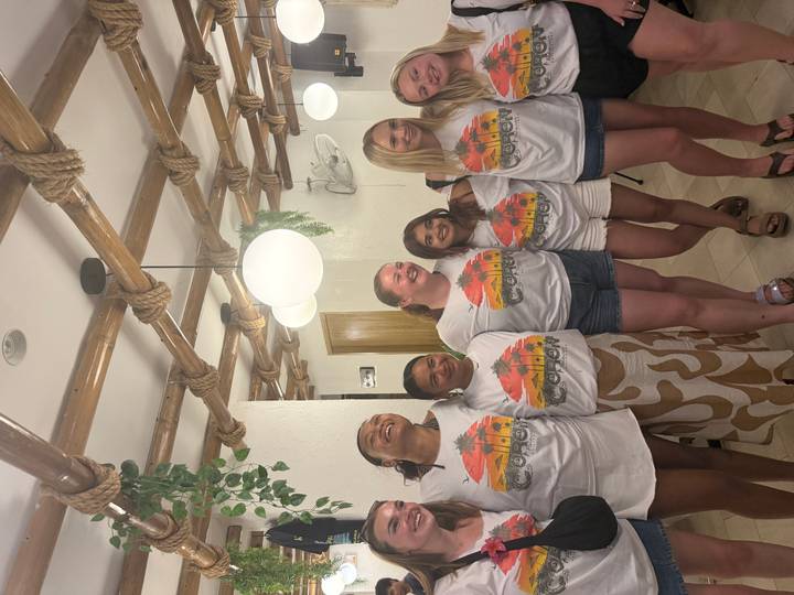Group of travellers wearing matching tour shirts pose indoors under bamboo ceiling decor.