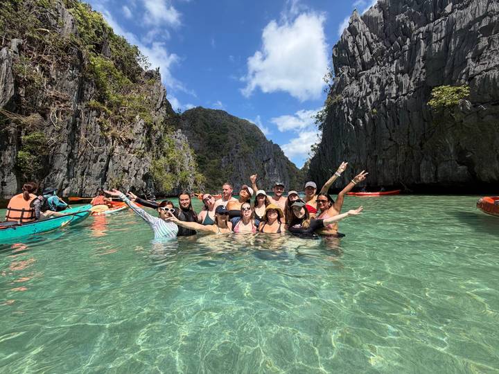 Group of friends pose waist-deep in turquoise lagoon framed by towering limestone cliffs.