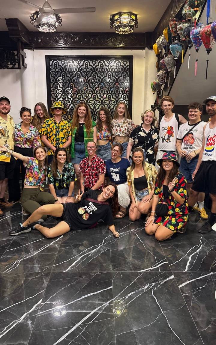 Large group wearing bright tropical shirts smiles for a fun indoor photo.