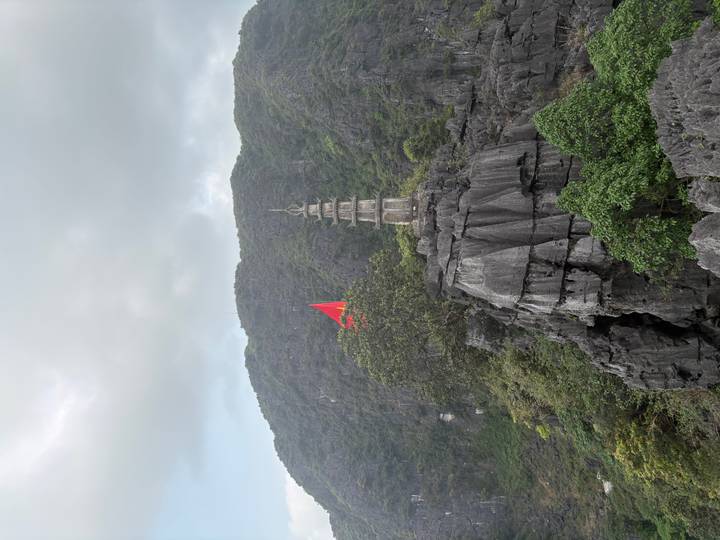 Stone pagoda and red flag sit atop a dramatic limestone karst overlooking green valleys.