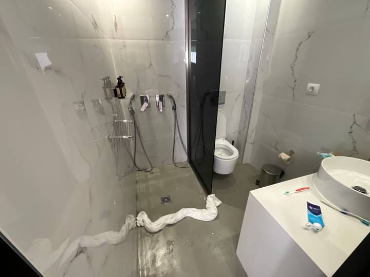 Modern bathroom with water leaking onto the floor and towels blocking the drain.