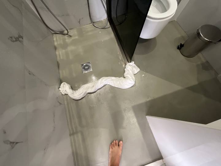 Close-up of flooded hotel shower floor with towel rolled to stop water spread.