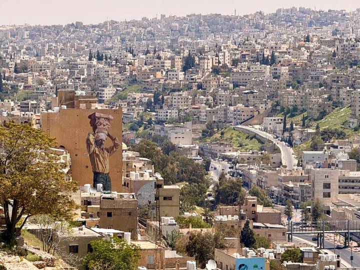 Panoramic view over Amman’s hillside neighborhoods with a large street-art mural of a photographer on a wall.