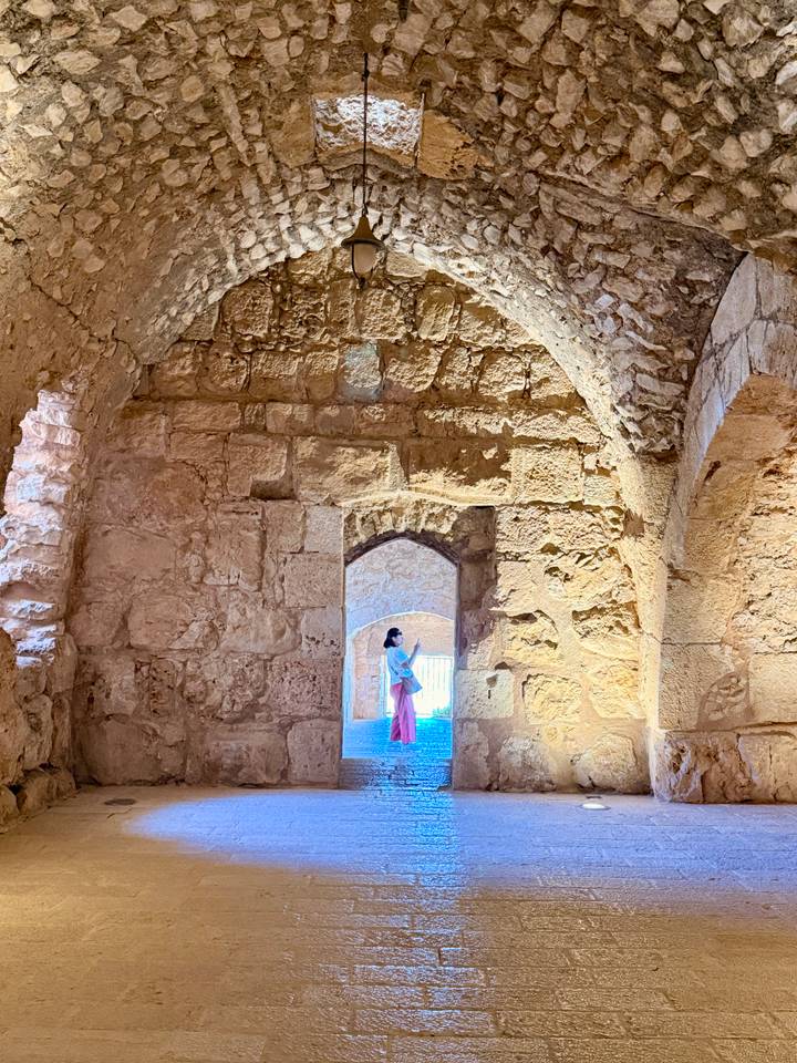 Woman in pink skirt admires light filtering through an ancient stone-arched chamber.