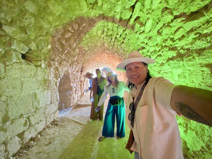 Selfie of four travellers inside a stone tunnel bathed in green and orange lighting.