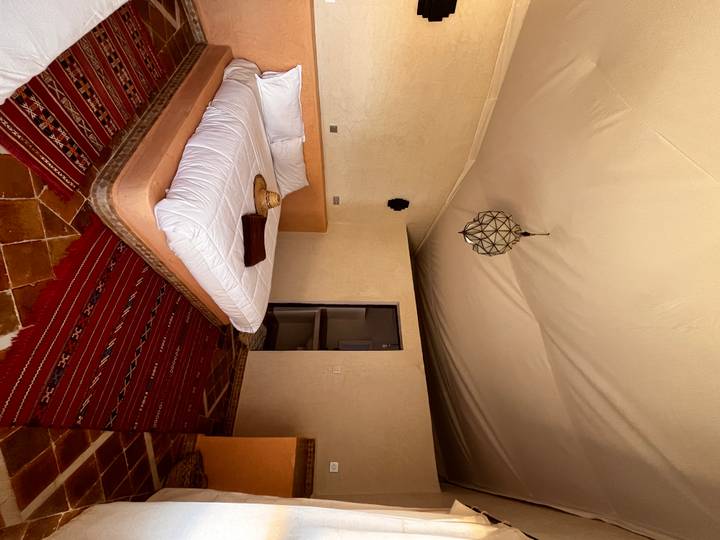 Rustic yet stylish desert-lodge bedroom with white linens, woven rug and straw hat on the bed.