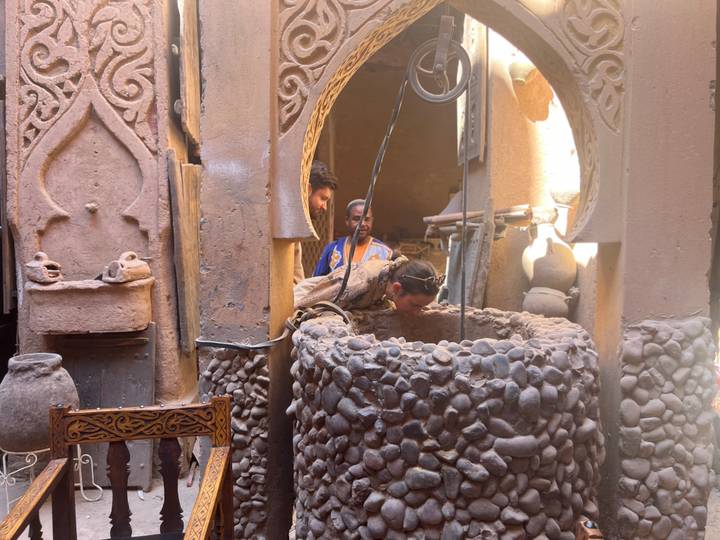 Visitors peer into a stone well inside an earthen, ornamented kasbah courtyard.