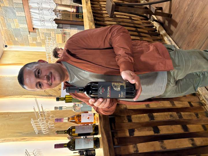 A smiling man in a winery proudly presents a bottle of Albanian red wine.