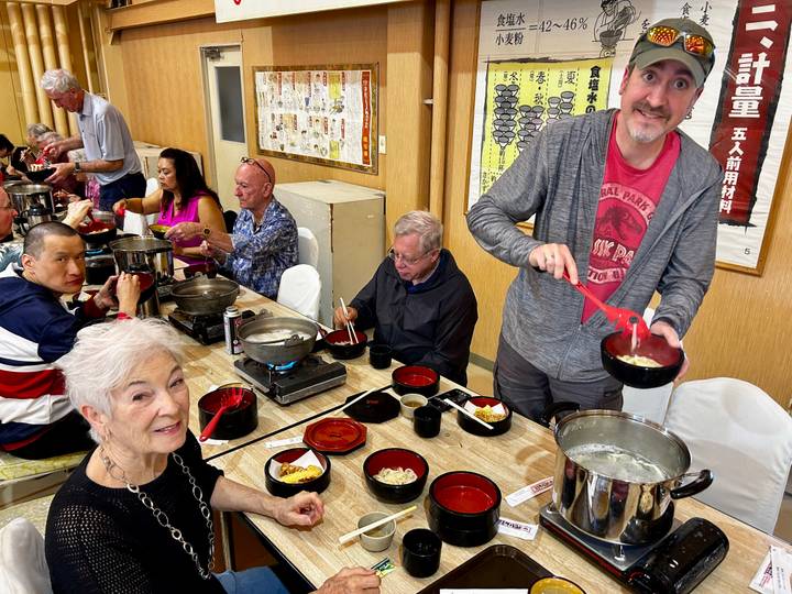 Travel group enjoys a hot-pot noodle meal at shared tables inside a Japanese restaurant.