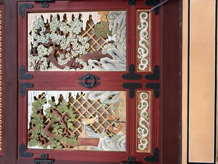 Intricately carved and painted wooden temple doors featuring trees, clouds and lattice patterns.