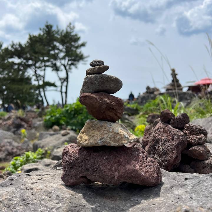 Small balanced stack of volcanic rocks with blurred natural background of shrubs and distant cairns.