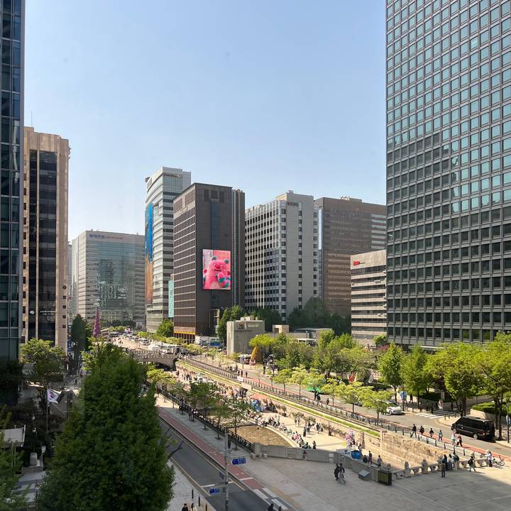Modern downtown skyline with tall glass buildings and a digital billboard above a tree-lined stream.