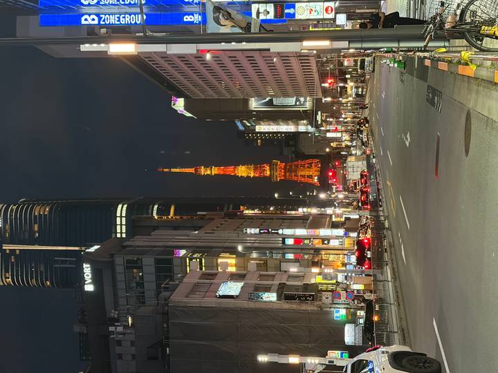 Night city street leading to the illuminated orange Tokyo Tower amid high-rise buildings.