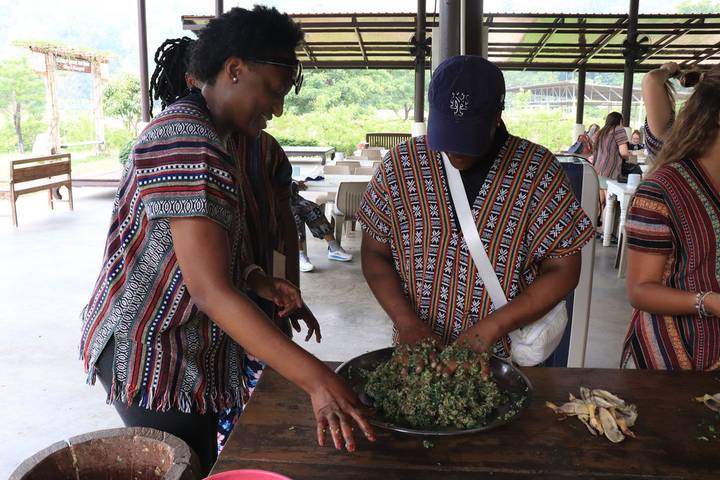 Participants wearing traditional patterned shirts preparing herbs in a cooking class pavilion.