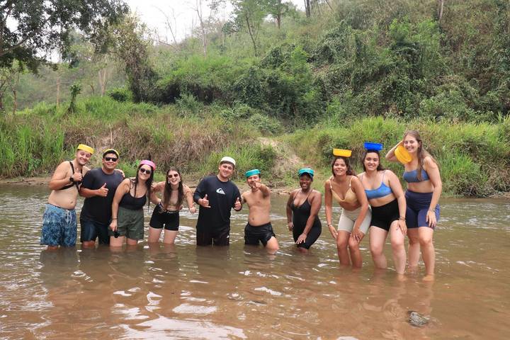 Group of young travellers standing knee-deep in a river giving thumbs-up during a water activity.