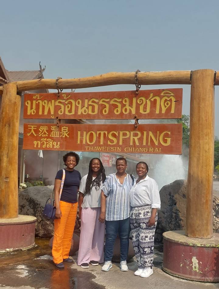 Four women posing beside a wooden signboard for a natural hot spring attraction.