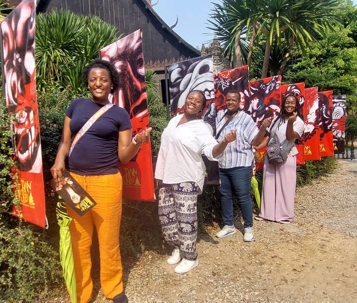 Group of travellers posing playfully beside colorful banner art along an outdoor walkway.
