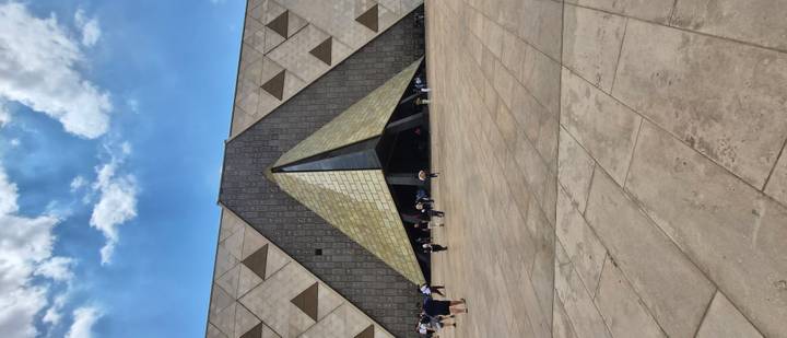 Visitors walk across the vast plaza of Egypt’s new Grand Museum with modern pyramid entrance.