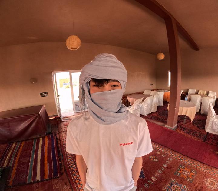 Young traveler indoors wearing traditional desert headscarf and white shirt.