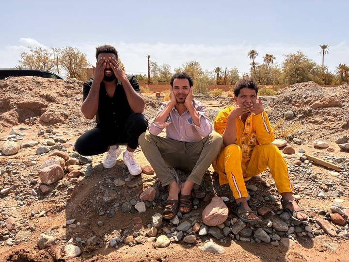 Three friends mimic see-no-evil pose while sitting on rocky desert ground.